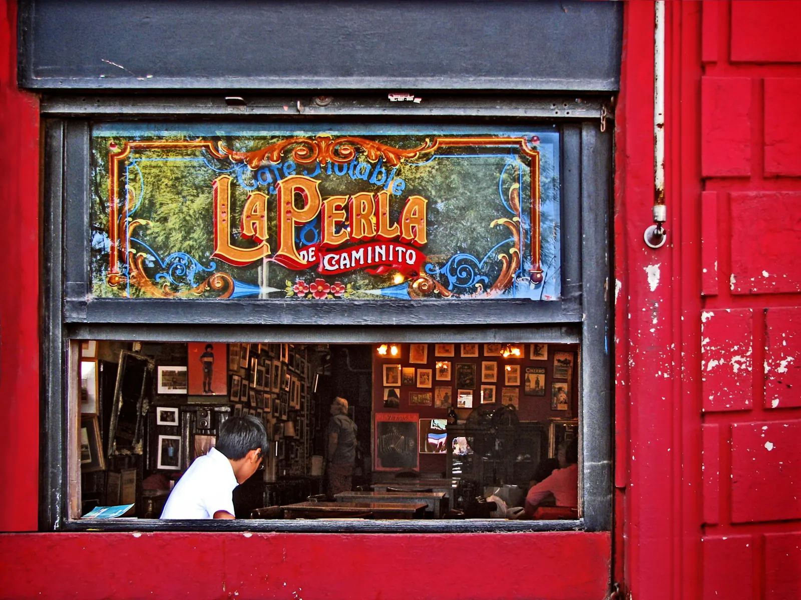 The vintage painted sign of the La Perla café on a red facade in Caminito, Buenos Aires