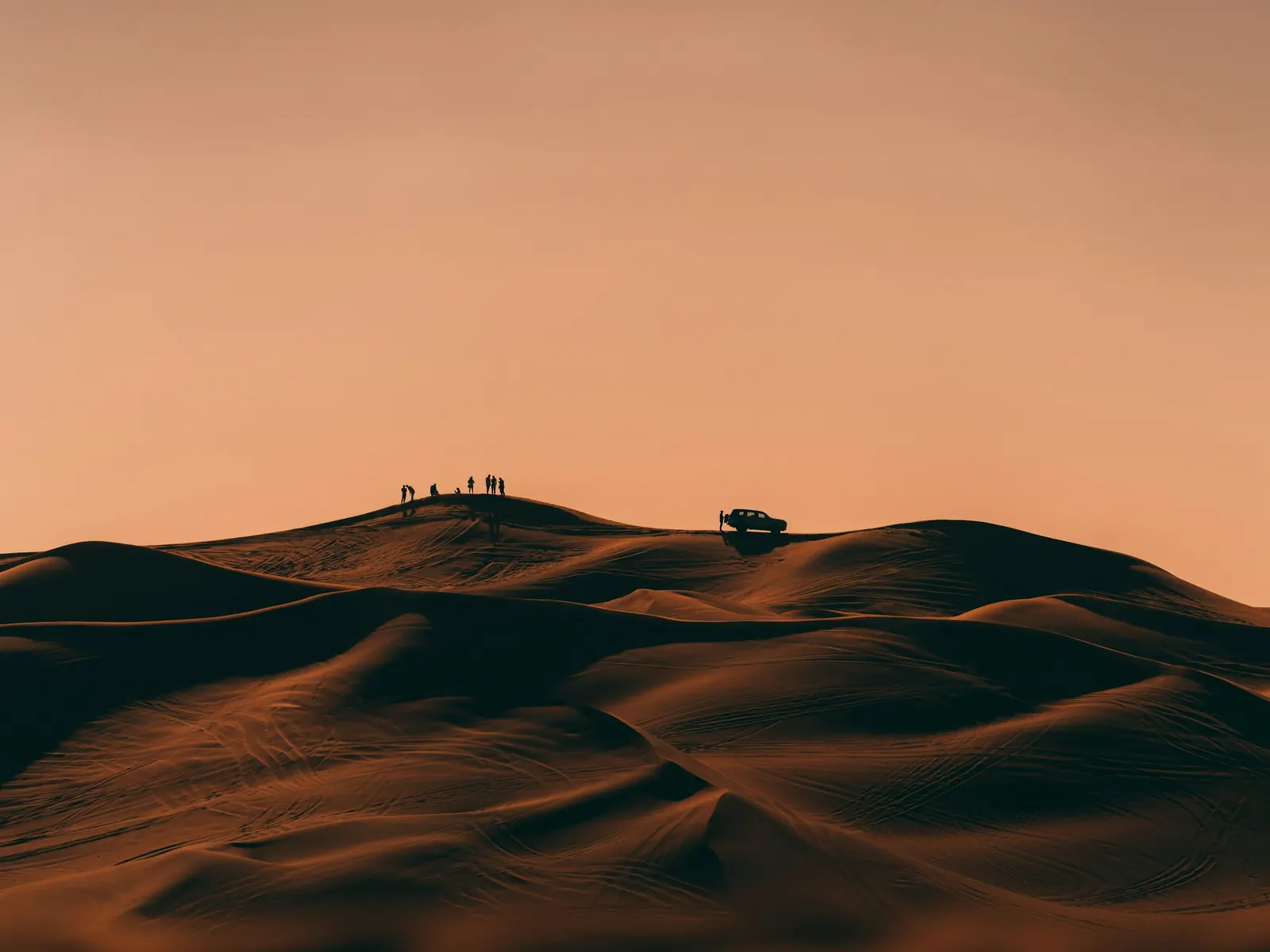A small group on a desert dune ridge beside a 4x4 at dusk near Dubai