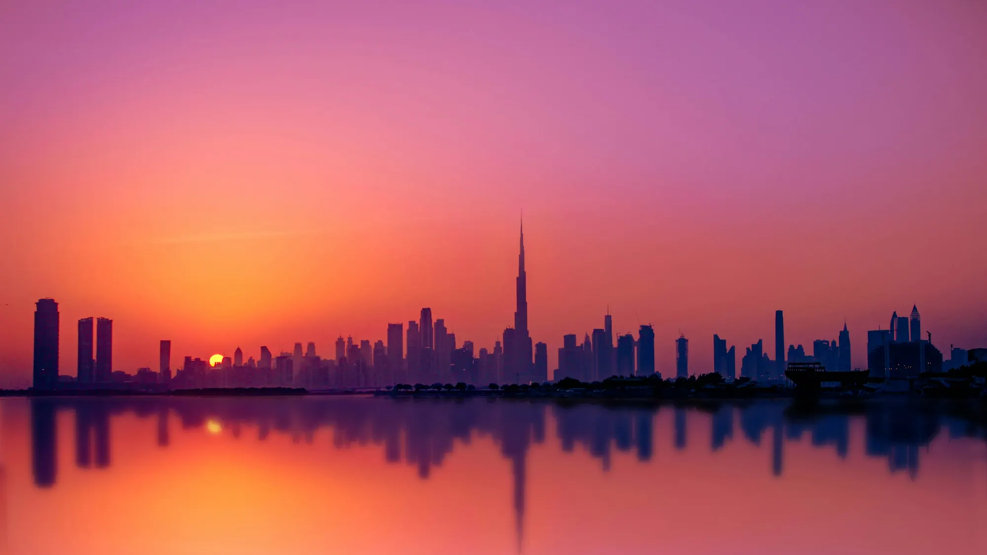 Dubai skyline with the Burj Khalifa silhouetted at sunset, mirrored in still water