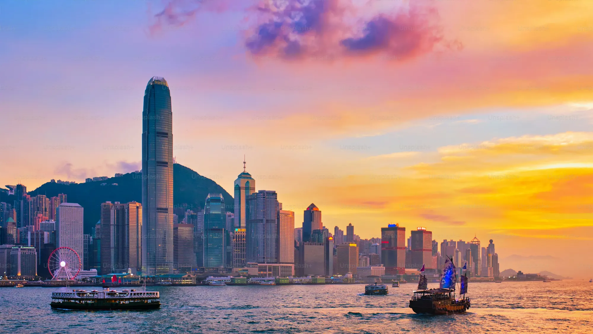 Hong Kong skyline across Victoria Harbour at sunset with a traditional junk boat